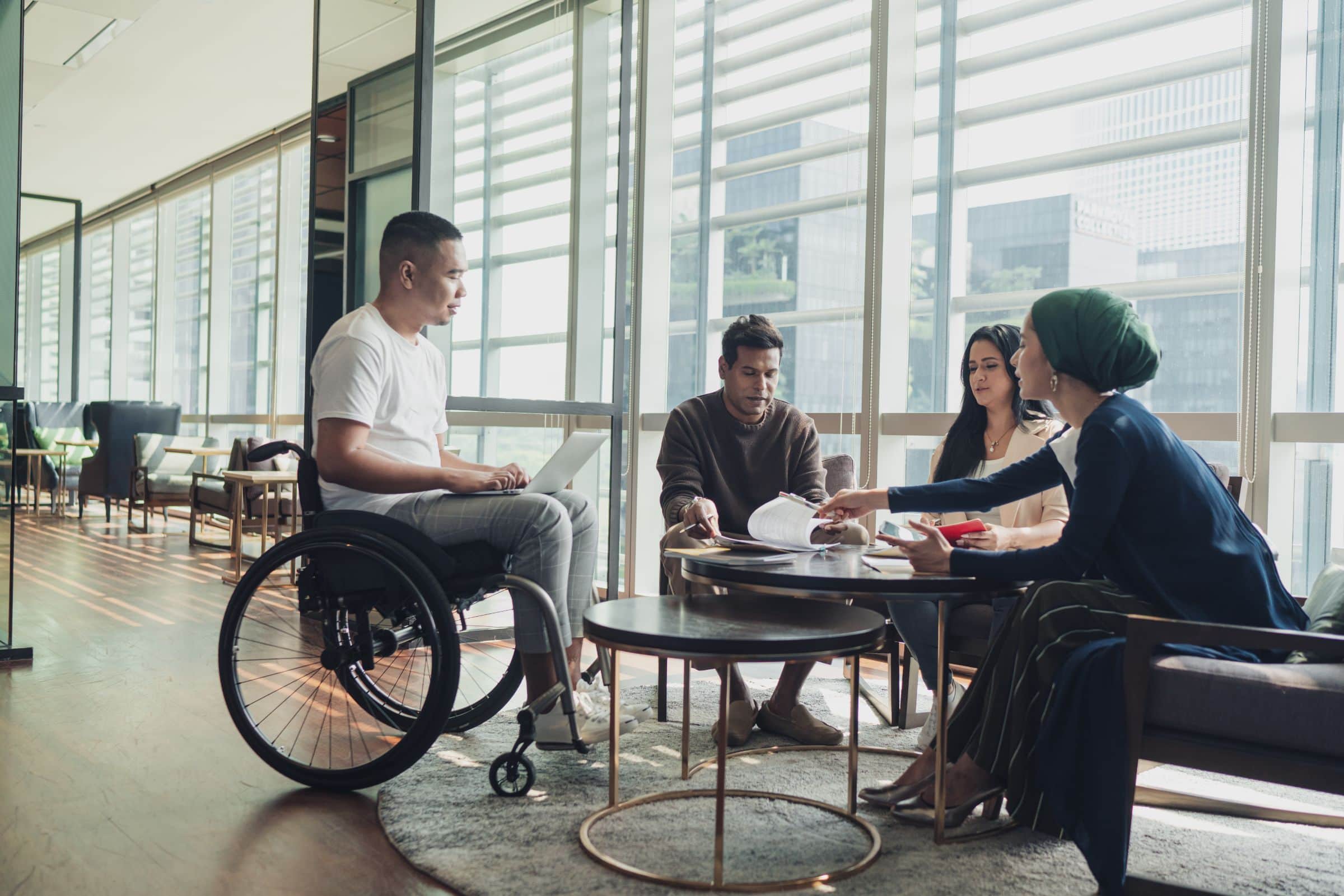 A wheelchair user with a laptop on his lap in a discussion with his colleagues 