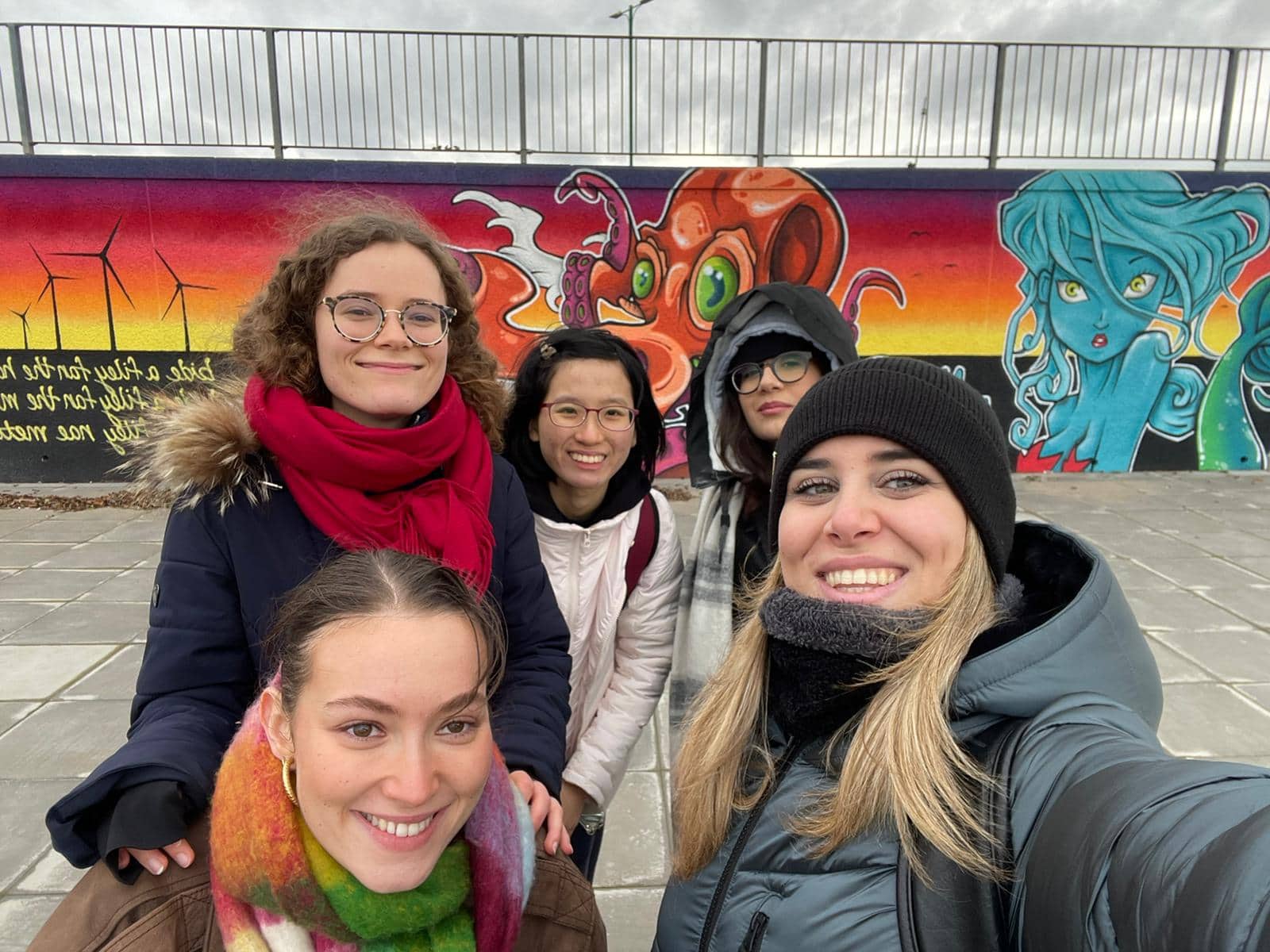 Jia Ying with some friends in winter wear in posing against a backdrop of street art.