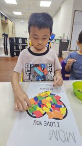 Celebrating Mums with Love and Learning at SPD 1 A young boy pasting coloured paper pieces to his handmade card