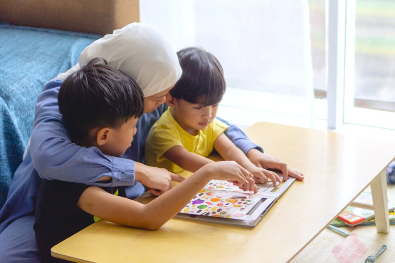 Experiencing Language - A Multisensory Approach to Language Learning 1 A mother reading with 2 boys, pointing to different illustrations on the book.