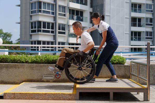 Celebrating Excellence: Lasting Impact of a Community Therapist – Pauline Koh 3 Pauline helps a client to do a wheelie down a step.