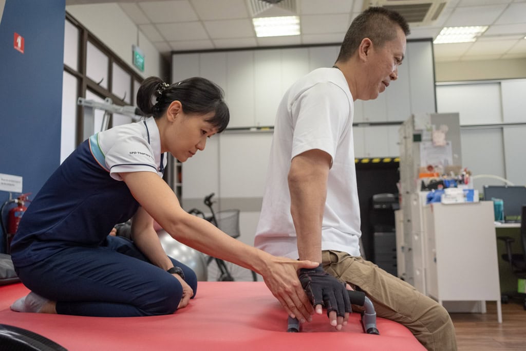 Celebrating Excellence: Lasting Impact of a Community Therapist – Pauline Koh 4 Pauline guiding from the back a client who is trying to lift himself using his arms.