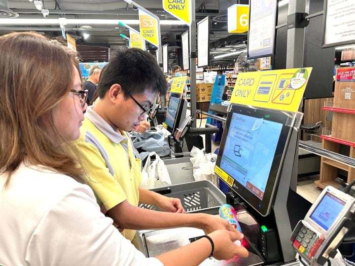 Vanessa guiding a D A C client in using a self checkout kiosk at a supermarket.