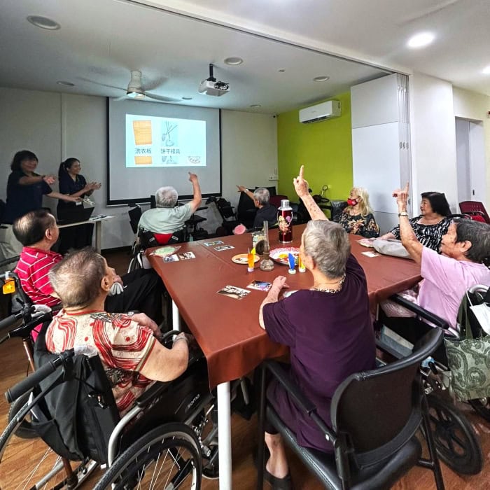 Seniors seated around a square table, several raise their hands to answer about a household item