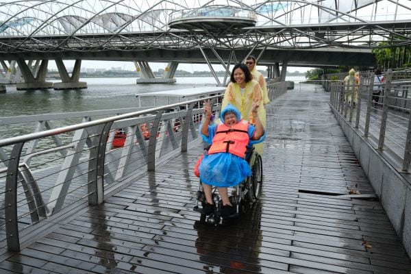Behind the scenes: Bringing an inclusive cruise ride to life at SPD Ability Walk 2025 6 An S P D client in raincoat smiling happily as she is pushed along by volunteers towards the cruise