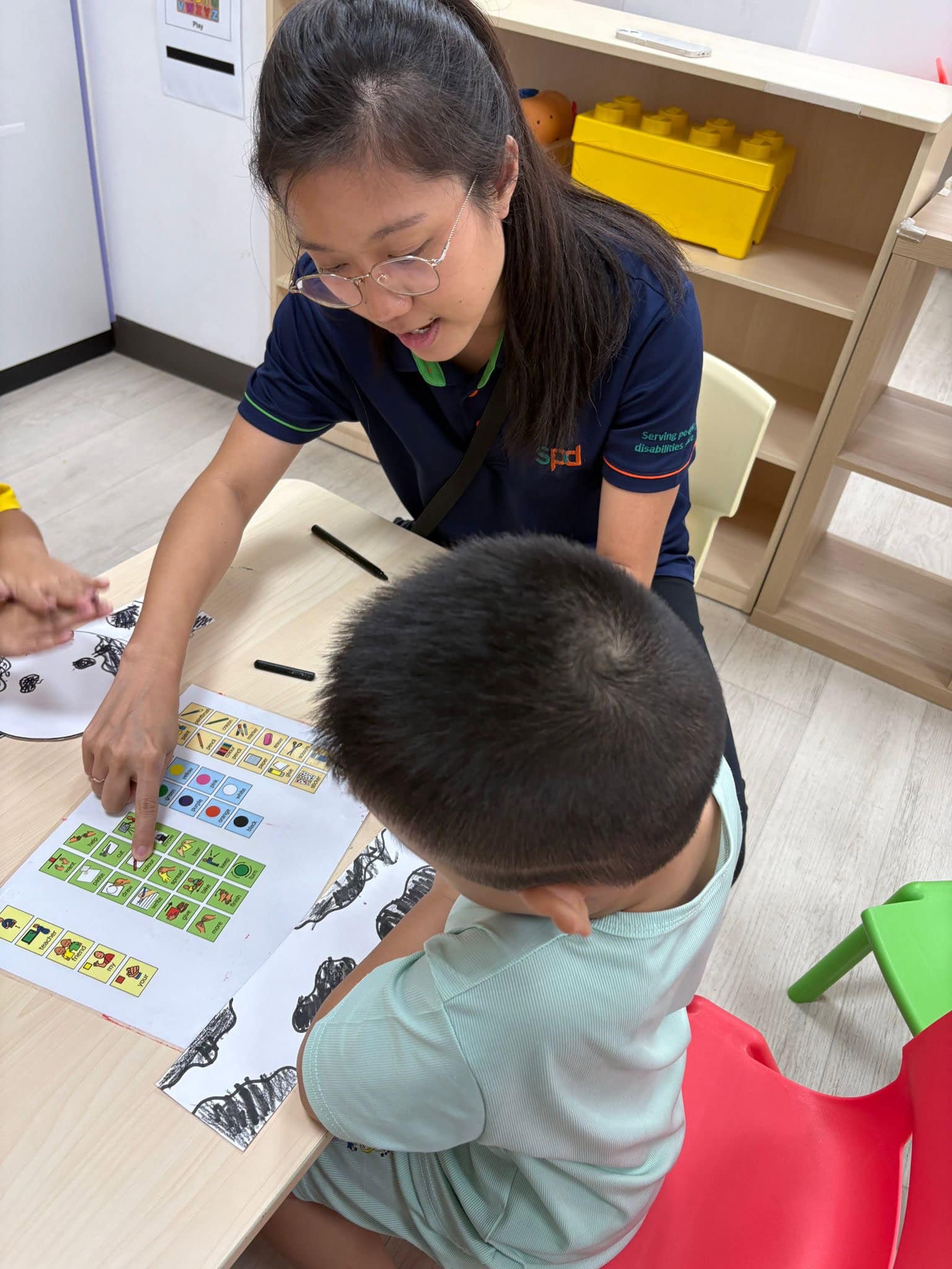 Jia Yi showing a young child how to communicate using an A A C chart.