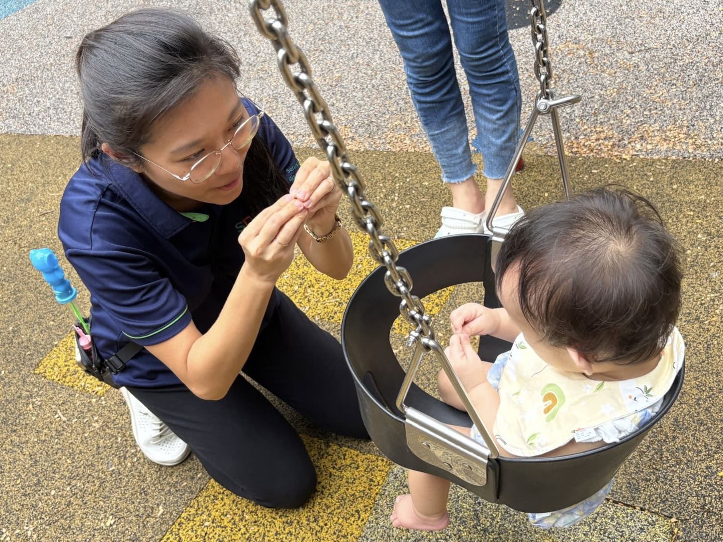 Jia Yi guides a child seated in a tyre swing to sign 'more'.