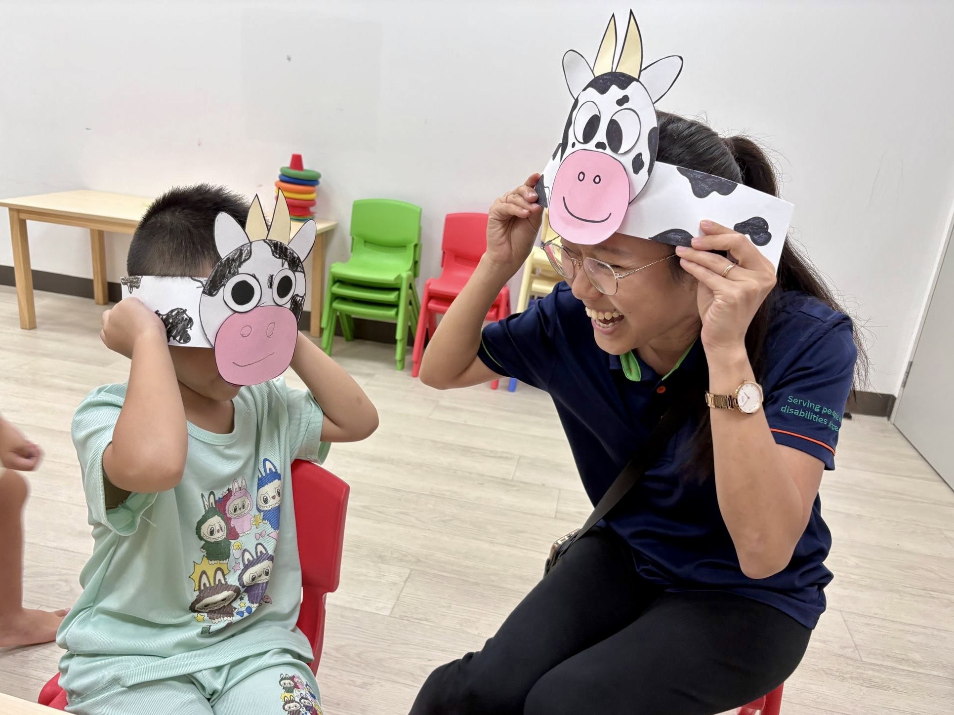 Jia Yi in an art and craft session with a young child wearing cows paper masks.