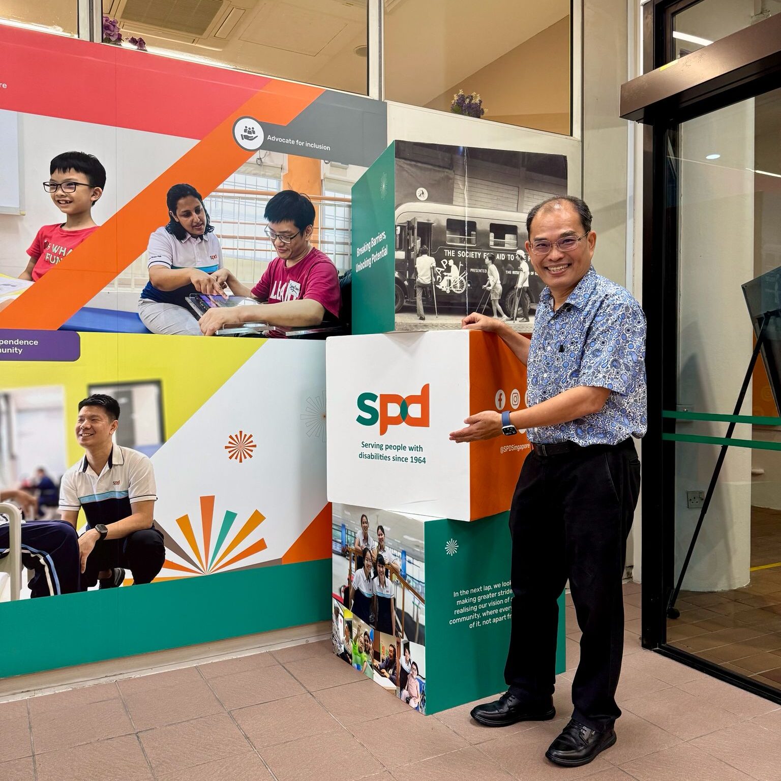 Mr Ong at the S P D Ability Centre lobby, posing with a cube with S P D's logo on it.