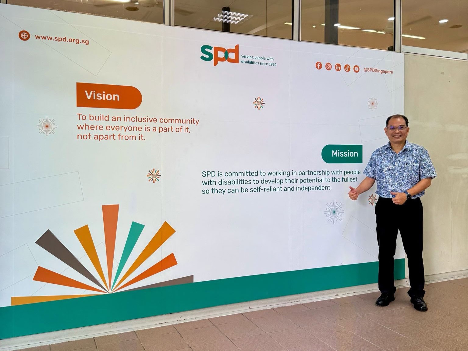 Mr Ong at S P D Ability Centre's lobby mural which shows the vision and mission.