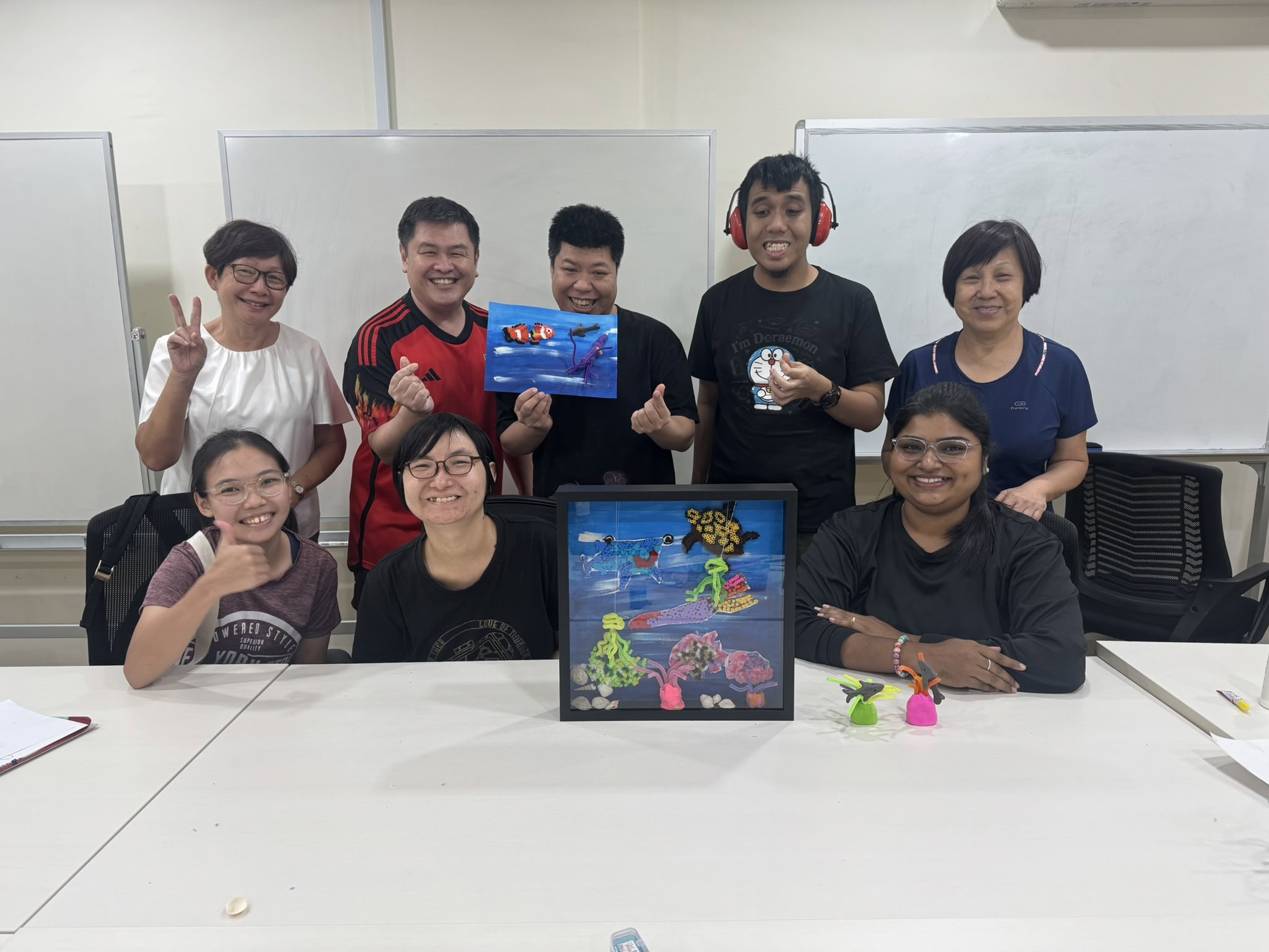 Strength in Community: She Came to Help Others and Found Support Herself 4 Sindhu with some colour craftwork framed up as tokens of appreciation, with her at the table are clients, volunteers and caregivers.