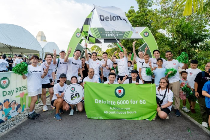 Deloitte runners at the end point of Deloitte 6000 for 60, waving their flag and looking happy.