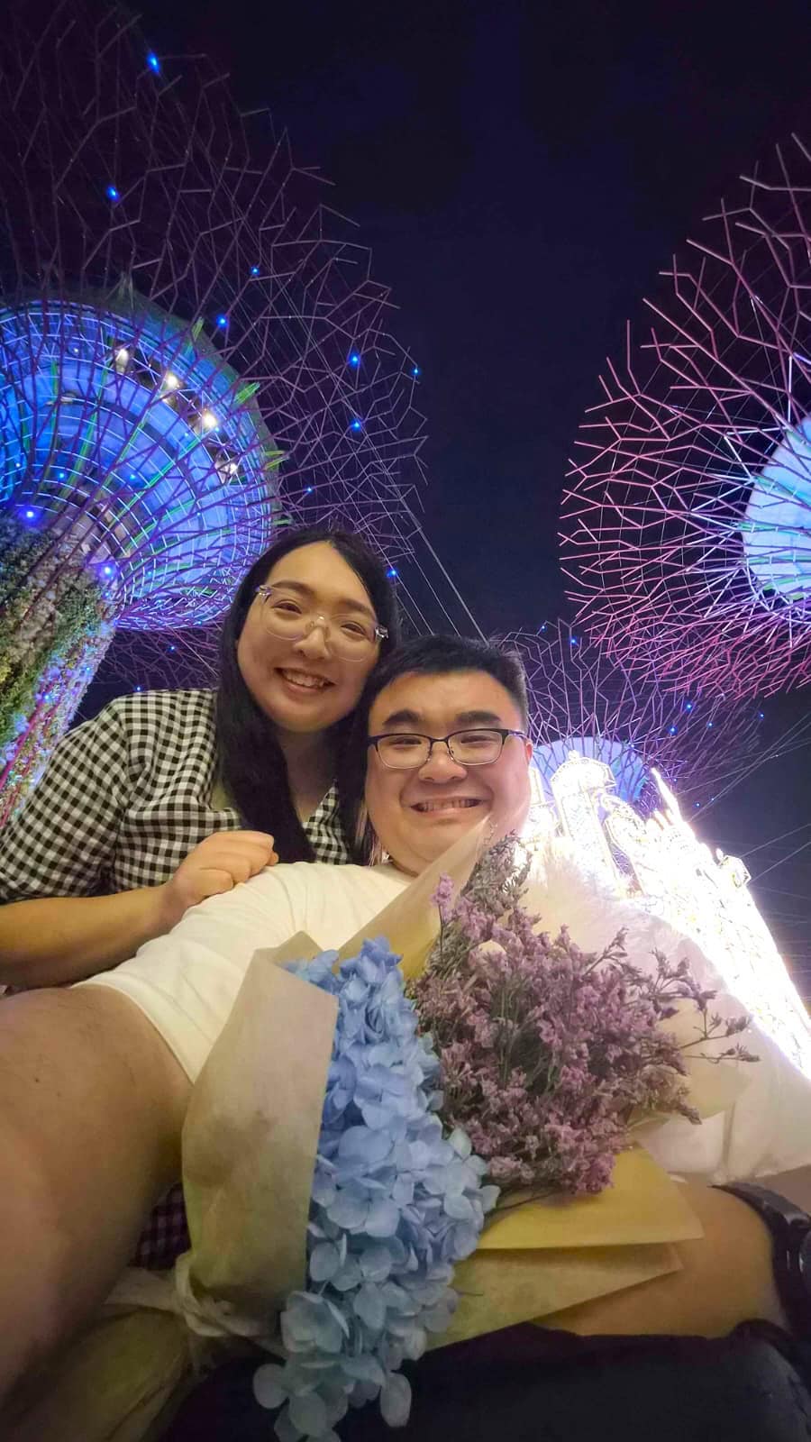 Kishon and Kelly smiling againstthe backdrop of the night sky and super trees at Gardens by the Bay