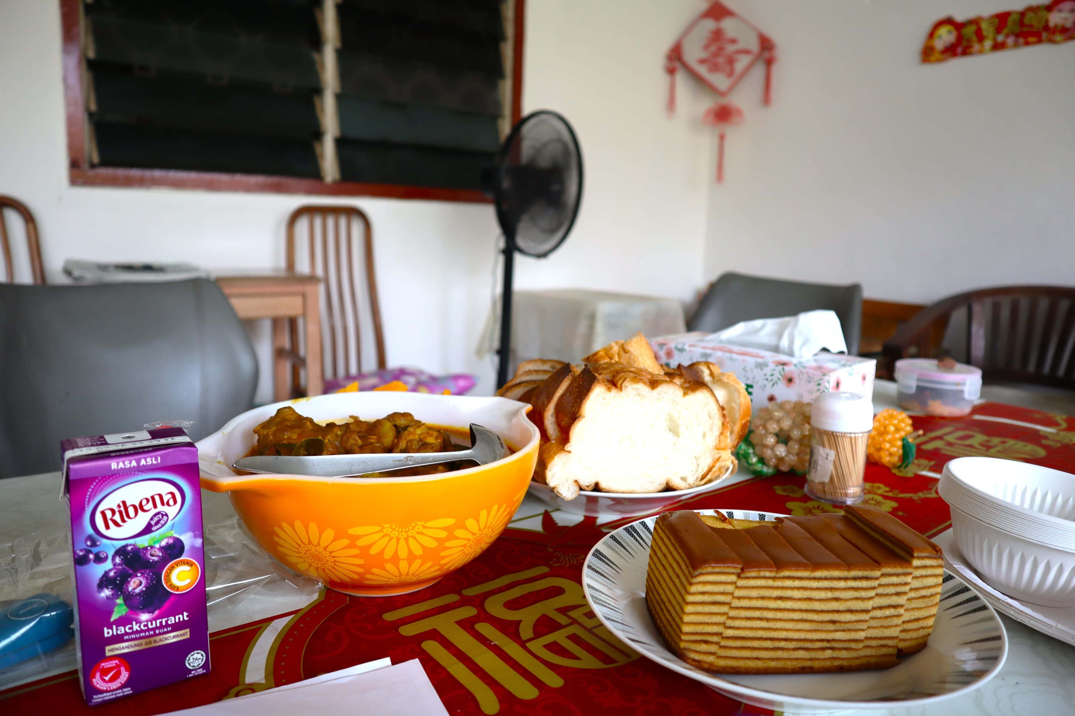A Heart That Never Grows Old: Auntie Molly’s volunteer journey with SPD 1 On the table is food Auntie Molly's helper prepared, including a juice box, a wbole of curry chicken, sliced french loaf and sliced kueh lapis
