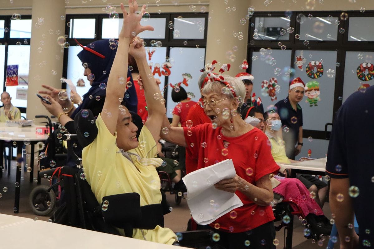 A Heart That Never Grows Old: Auntie Molly’s volunteer journey with SPD 6 Auntie Molly singing enthusiastically with a D A C client who is in a wheelchair. Bubbles are in the fore- and background.