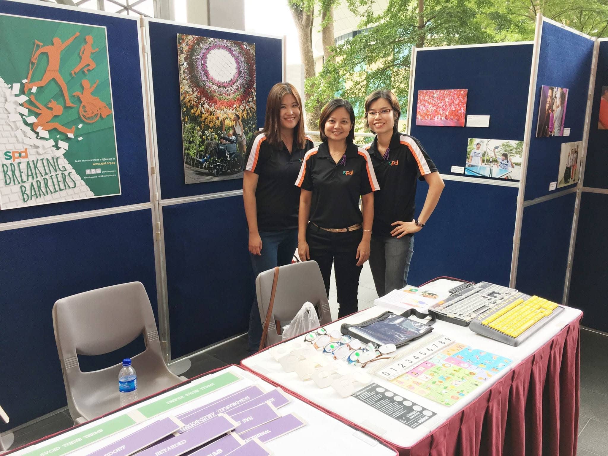 Sharon standing at a booth in an event together with 2 colleagues