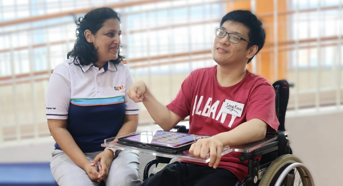 An SPD staff interacting with a SATC client seated on a wheelchair and using a tablet