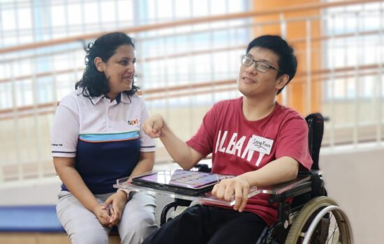 An SPD staff interacting with a SATC client seated on a wheelchair and using a tablet
