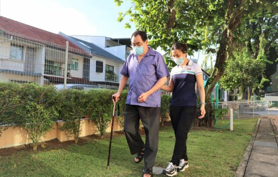 S P D professional supporting an elderly man walking with a walking stick by holding onto his elbow