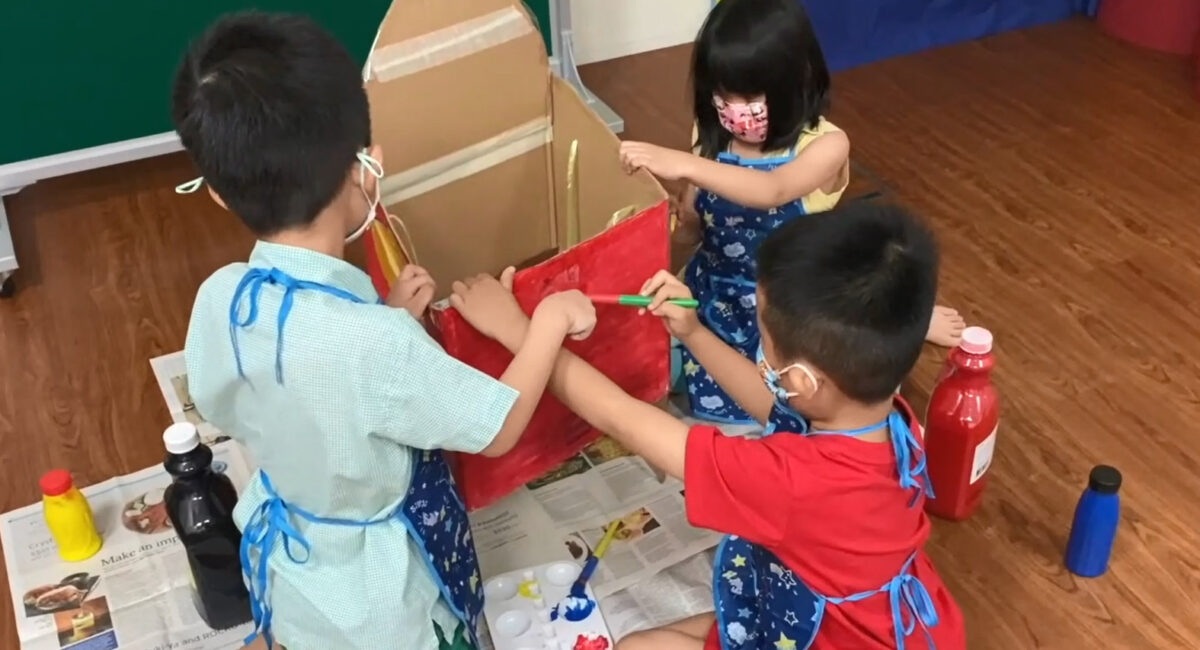 Three children using watercolour to paint a box