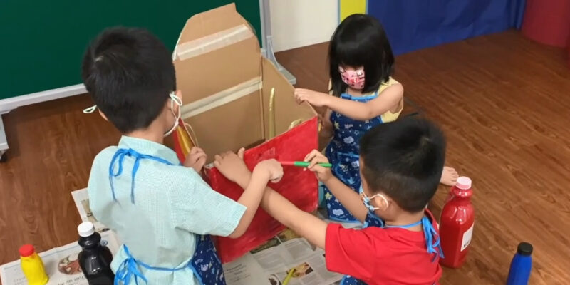 Three children using watercolour to paint a box