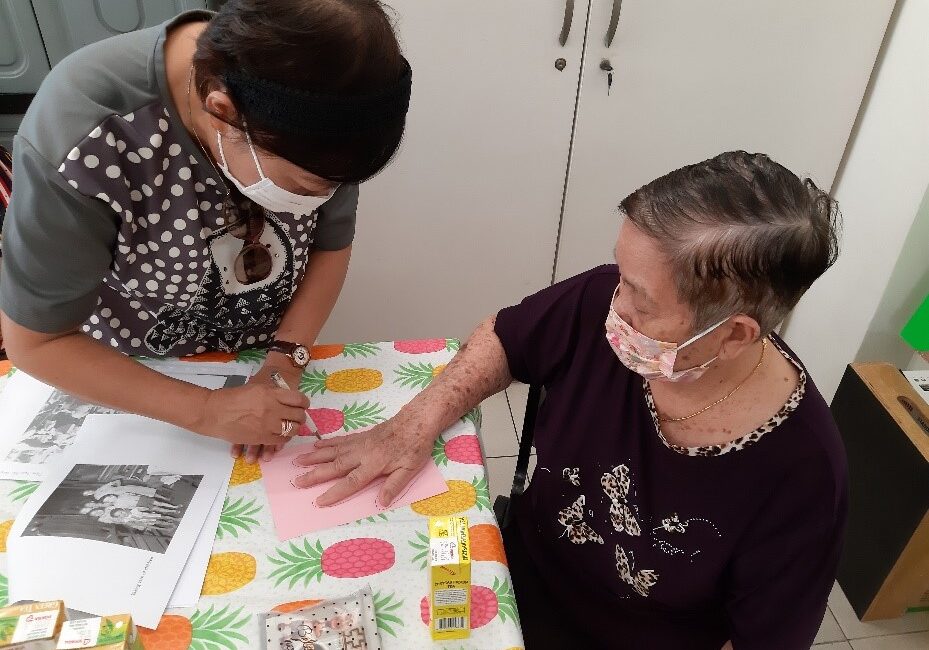 Volunteer helping an elderly client trace her hand on a pink piece of paper