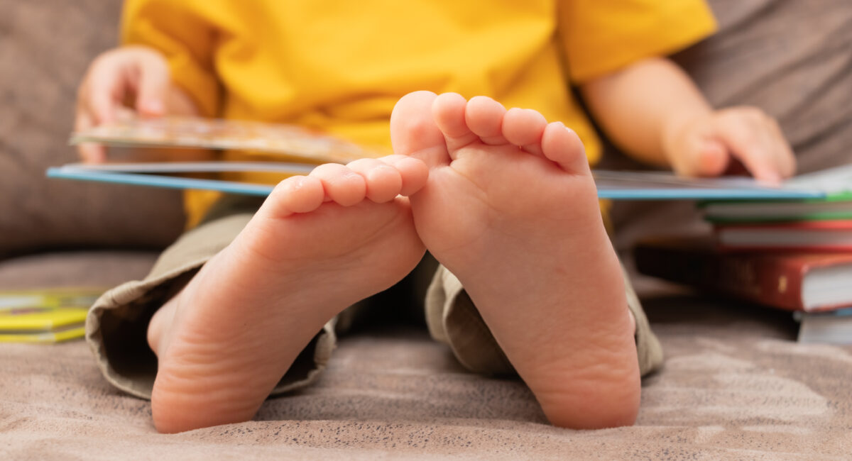 A photo of a child holding an open book, with his feet propped up in the foreground of the photo
