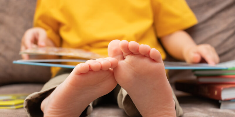 A photo of a child holding an open book, with his feet propped up in the foreground of the photo