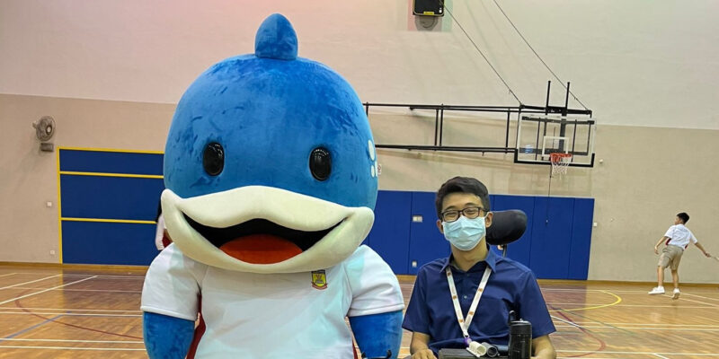 Mr Wong seated in his wheelchair beside a blue whale mascot