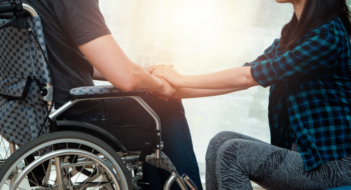 A lady holding the hands of her spouse who is using a wheelchair