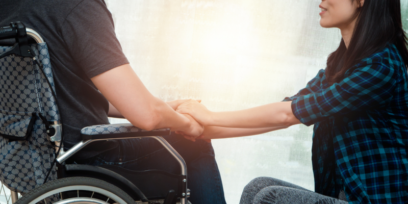 A lady holding the hands of her spouse who is using a wheelchair