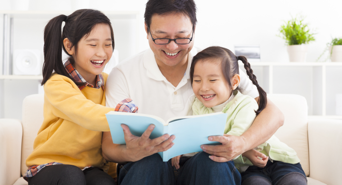 A father reading together with his two young daughters