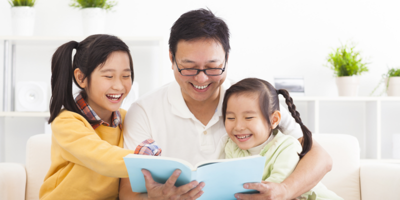 A father reading together with his two young daughters