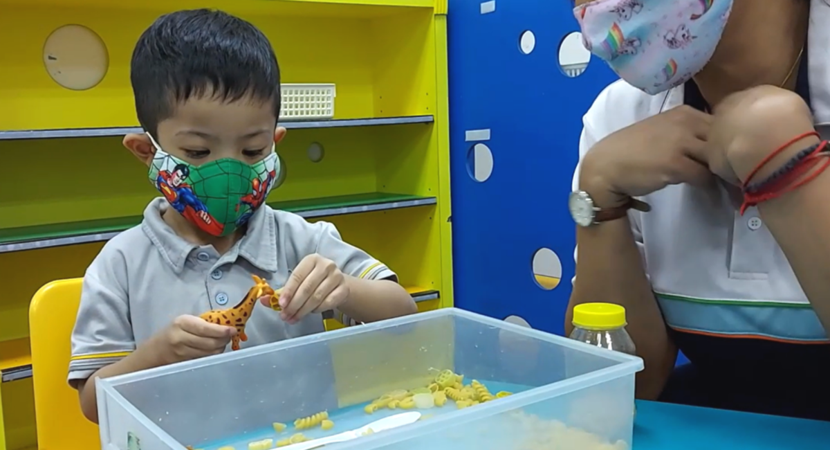 A young boy playing with his toys with his teacher by his side