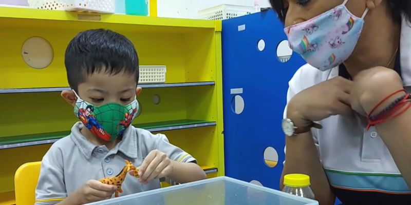 A young boy playing with his toys with his teacher by his side
