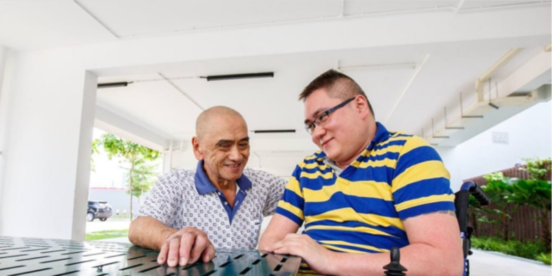 Mr Kua sitting on a bench at the void deck with his stepson Mr Lim, who is using a wheelchair
