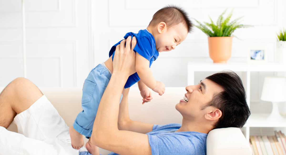 A dad lying on the sofa while lifting his young son up in the air