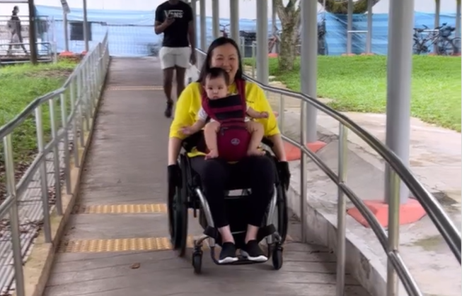 Jean using a carrier to carry Evan as she goes down the slope on her wheelchair
