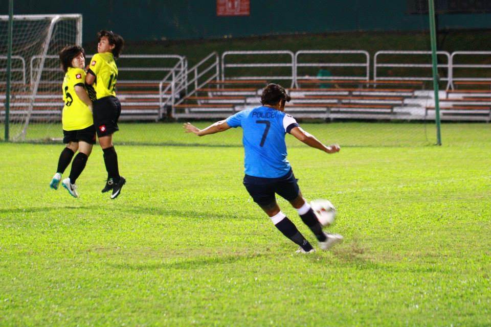 Rena and Shahidah in yellow jerseys jumping together as a wall to block a free kick from an opponent wearing blue