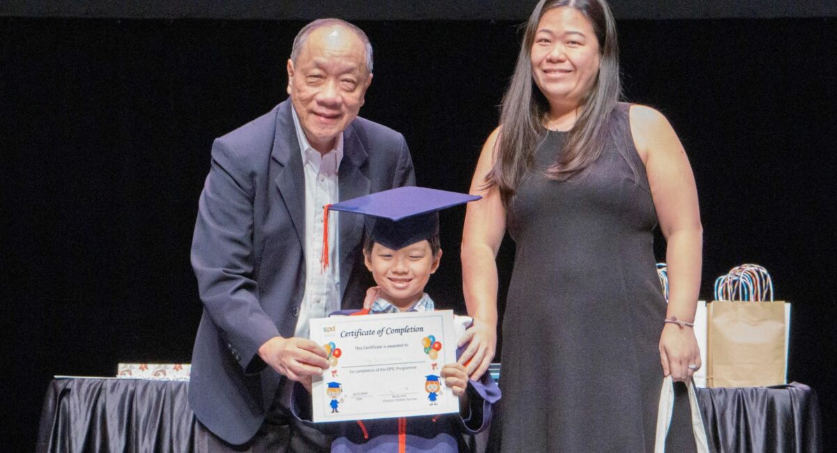Prof Ho at the EIPIC graduation ceremony 2019, handing a certificate to a boy in graduation gown and his mother