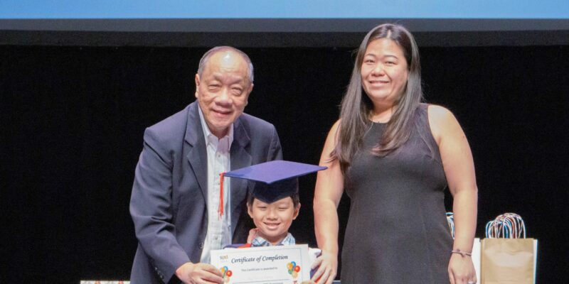 Prof Ho at the EIPIC graduation ceremony 2019, handing a certificate to a boy in graduation gown and his mother