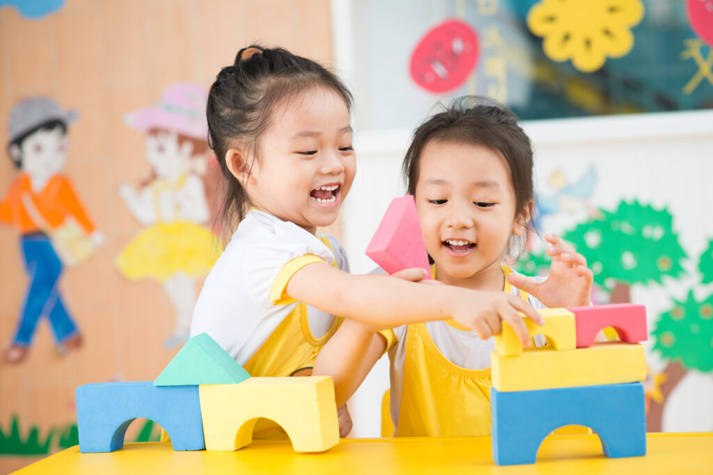 2 girls happily playing with building blocks