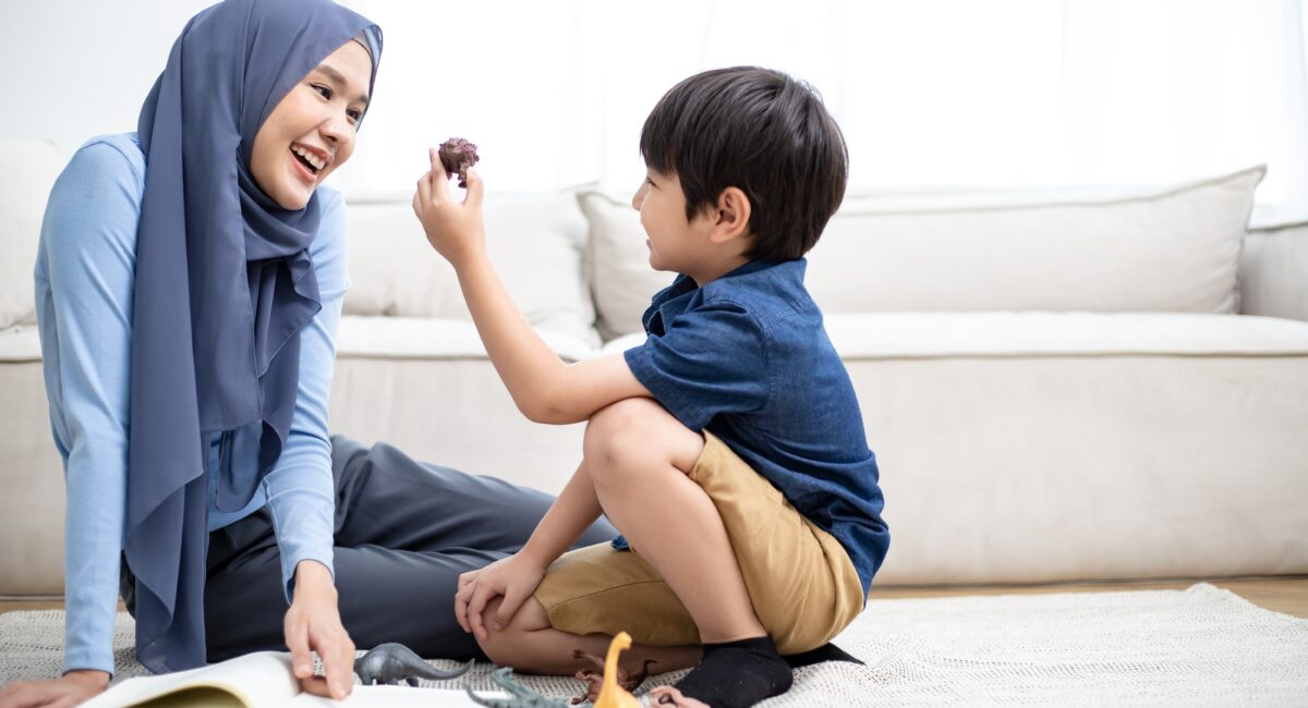 A mother smiling at her son as he holds up a small dinosaur toy