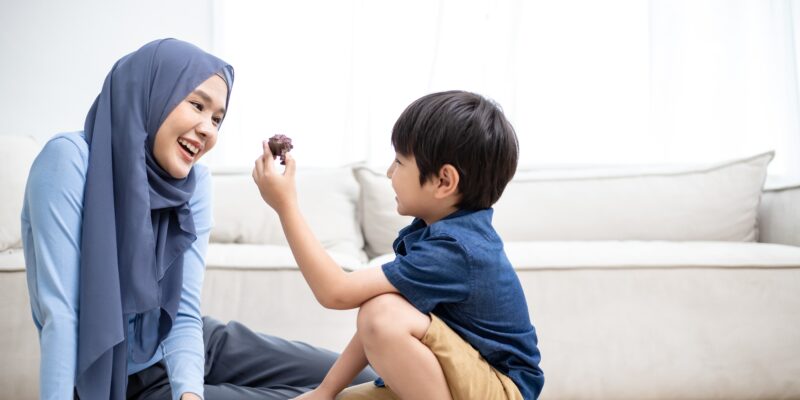 A mother smiling at her son as he holds up a small dinosaur toy