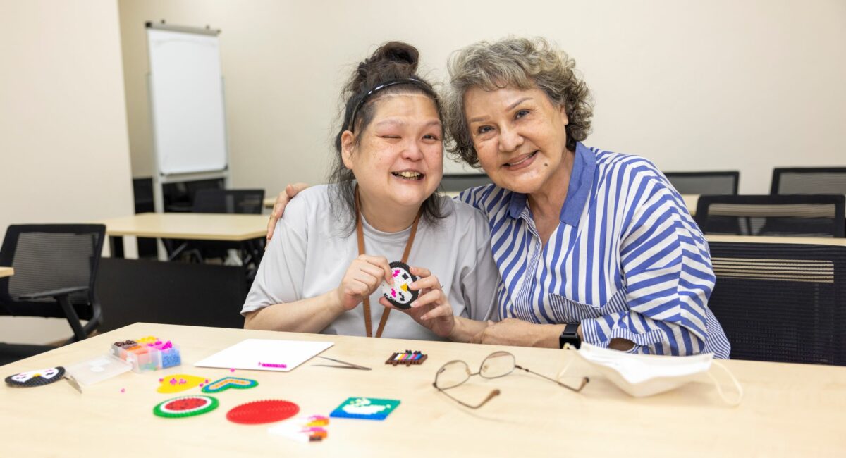 Veronica and mum Mdm Lydia smiling, a table of craft items scattered on the table they are at