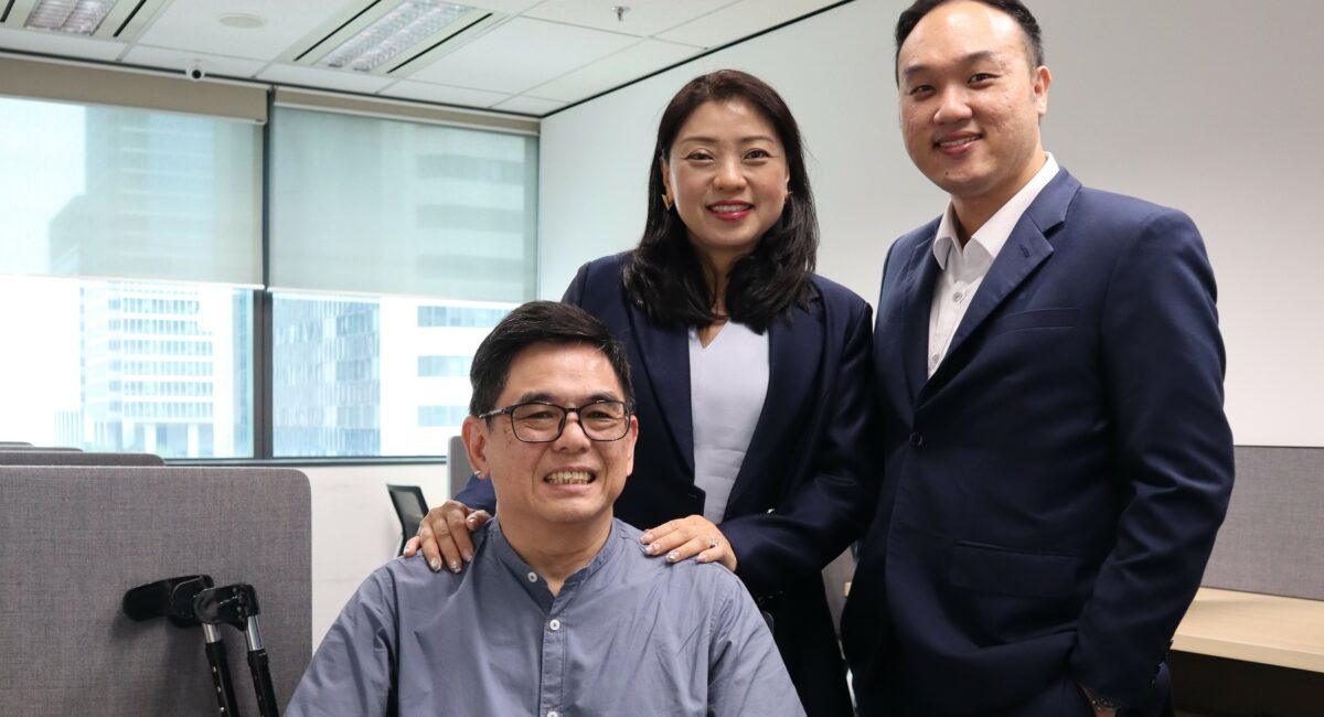 Mr Chong at seated at his desk with the founder of MCS Advisory Group Ms May Chan, and his manager and direct supervisor Mr Daniel Chong