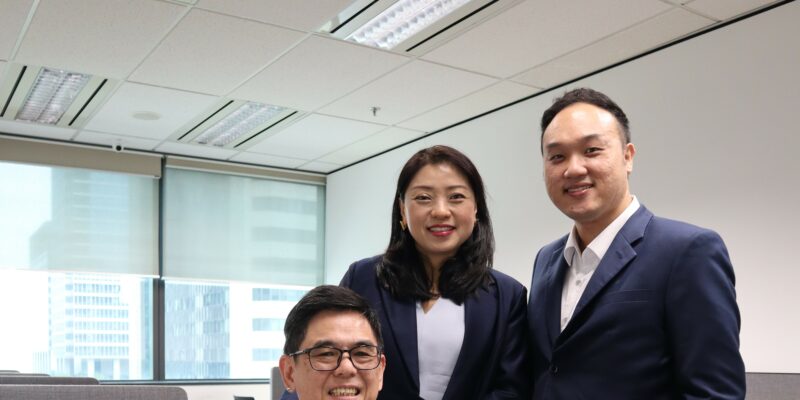 Mr Chong at seated at his desk with the founder of MCS Advisory Group Ms May Chan, and his manager and direct supervisor Mr Daniel Chong