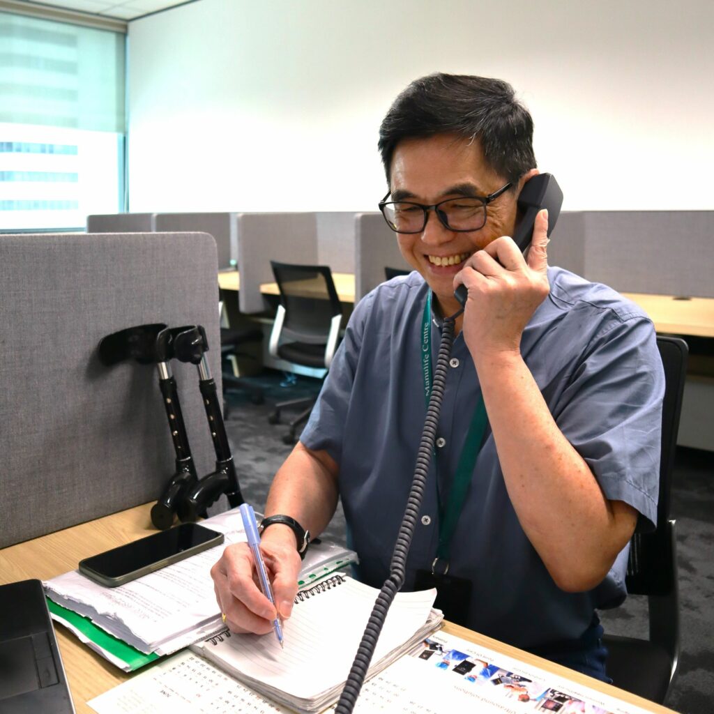 Mr Chong at his desk, smiling as he speaks into a telephone.
