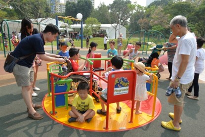 Several children playing on a roundabout at Bishan-Ang Mo Kio Inclusive Playground as 2 adults look on