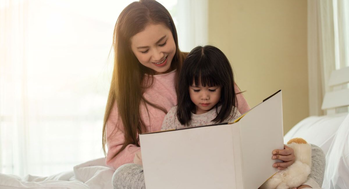A mother reading a book with her daughter on a bed